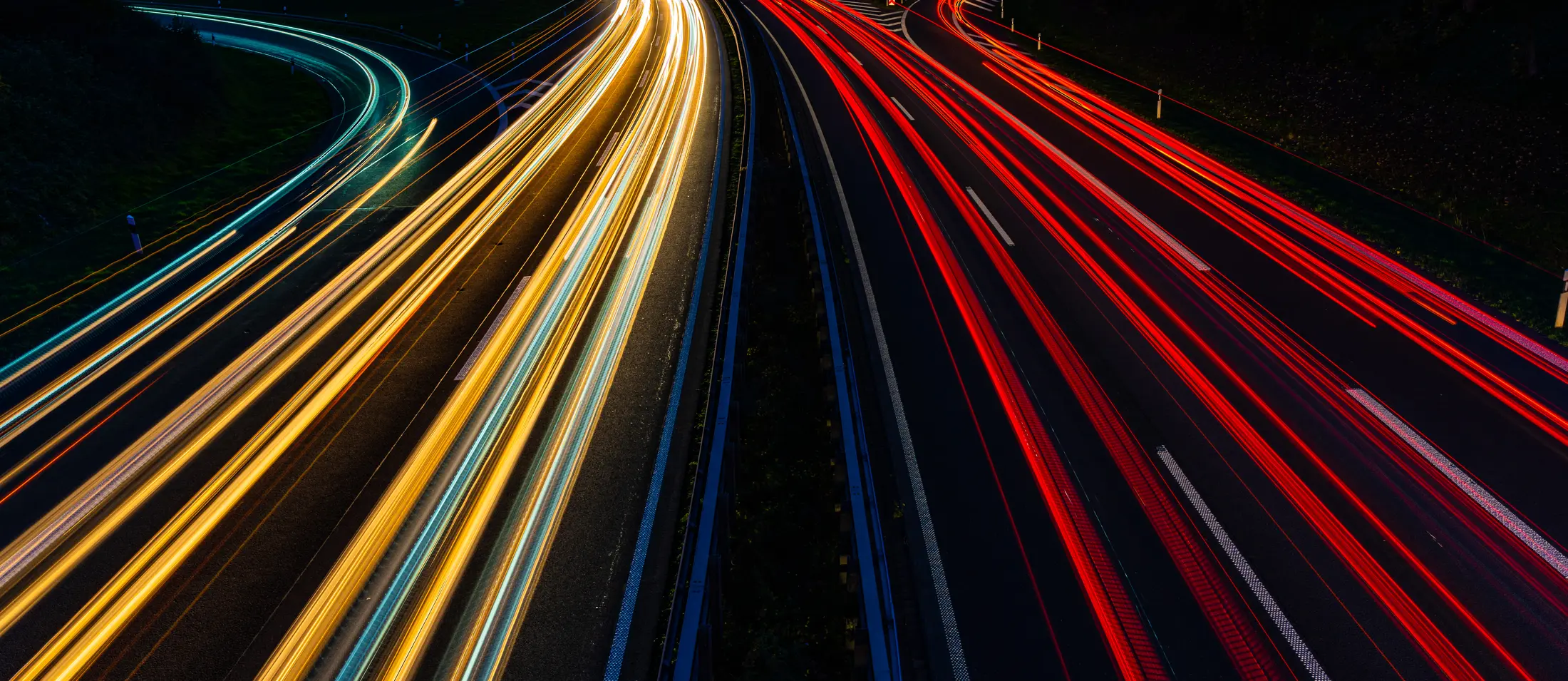 A long exposure of a road at night, headlights streaming away on one side and tail lights coming back on the other