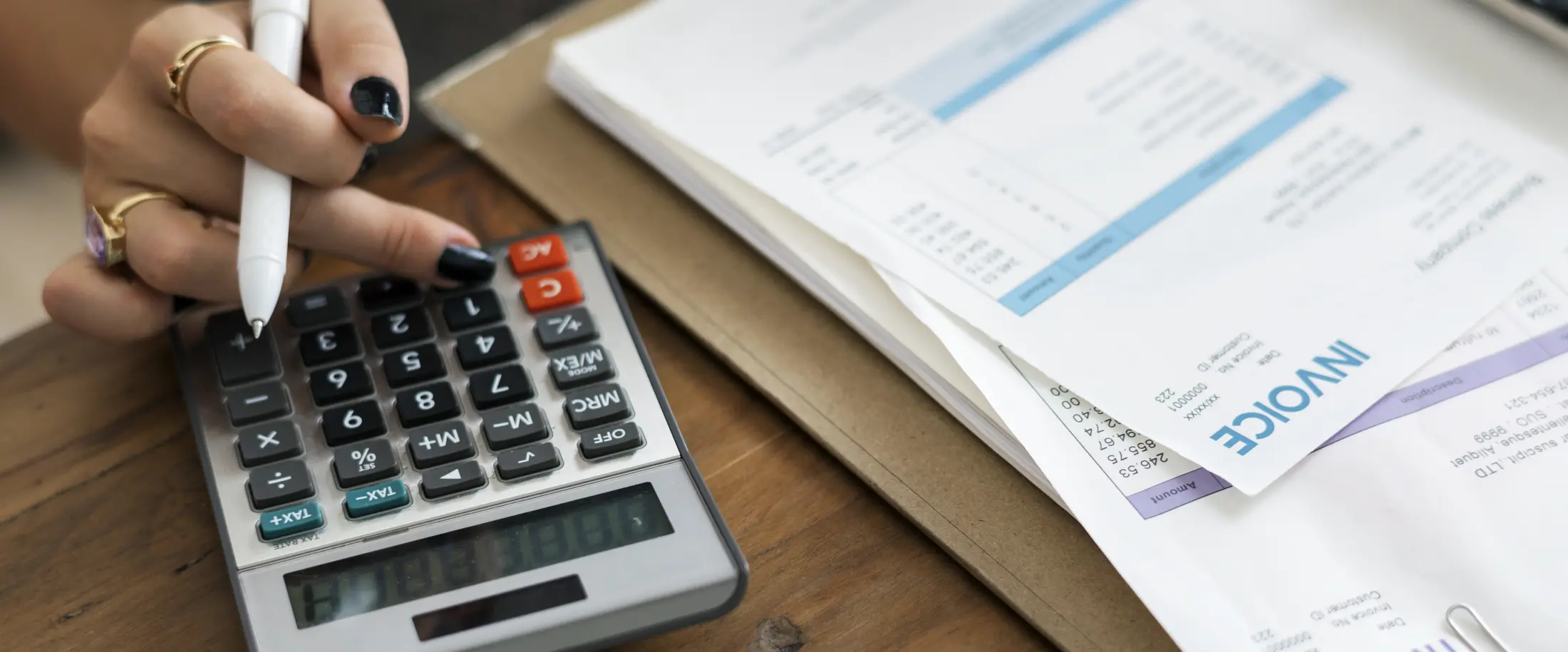 A hand working a calculator beside a stack of unpaid invoices