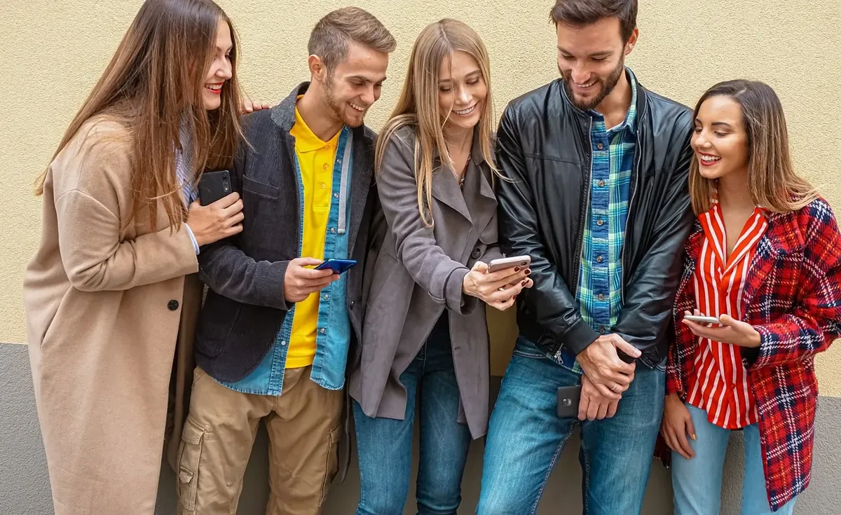 A group of young people standing next to each other looking at each others smartphone.