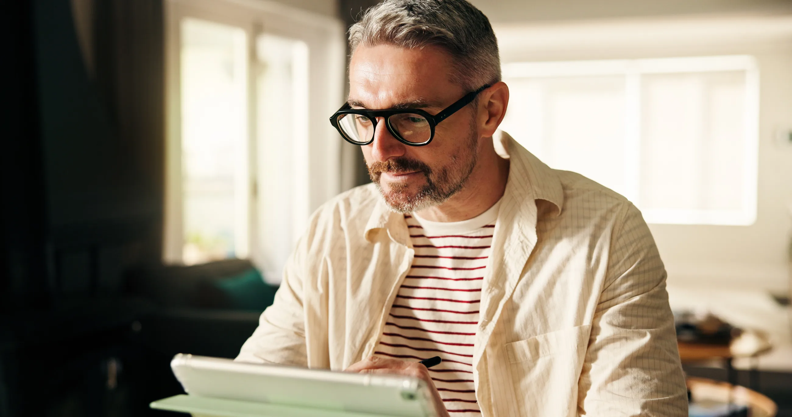 A man reading an article on a tablet by a sunny window